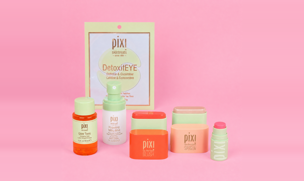Pixi skincare set arranged on a pink background, including a DetoxiEYE pouch, cleansing wipes, blush, superglow, toner, serum, and a lip treatment. The products feature pastel and bright colors like orange, coral, mint green, and peach.