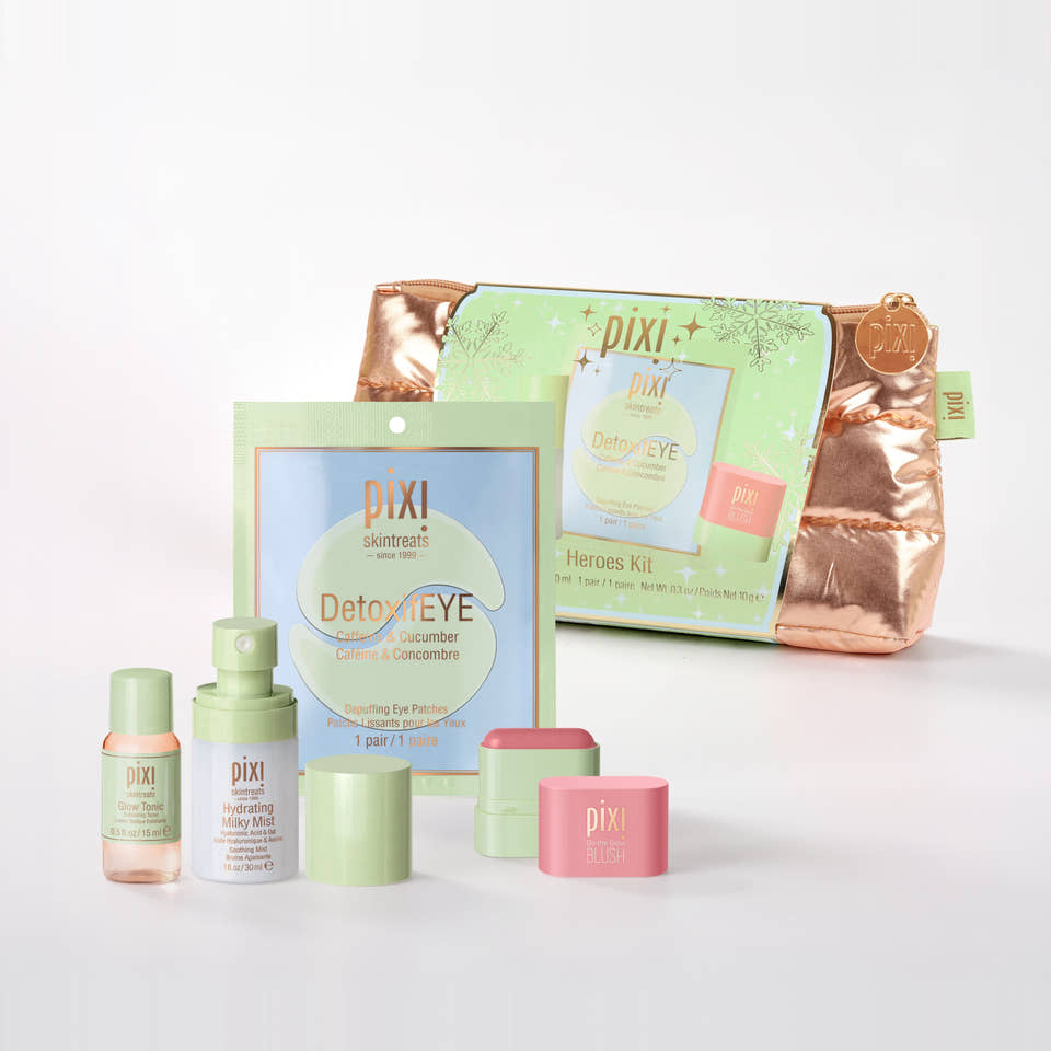 Pixi Heroes Kit skincare set on a clean white background, featuring a metallic rose gold zippered pouch, a light green sachet, a small pink jar, a light green bottle, and other matching skincare containers. view 1