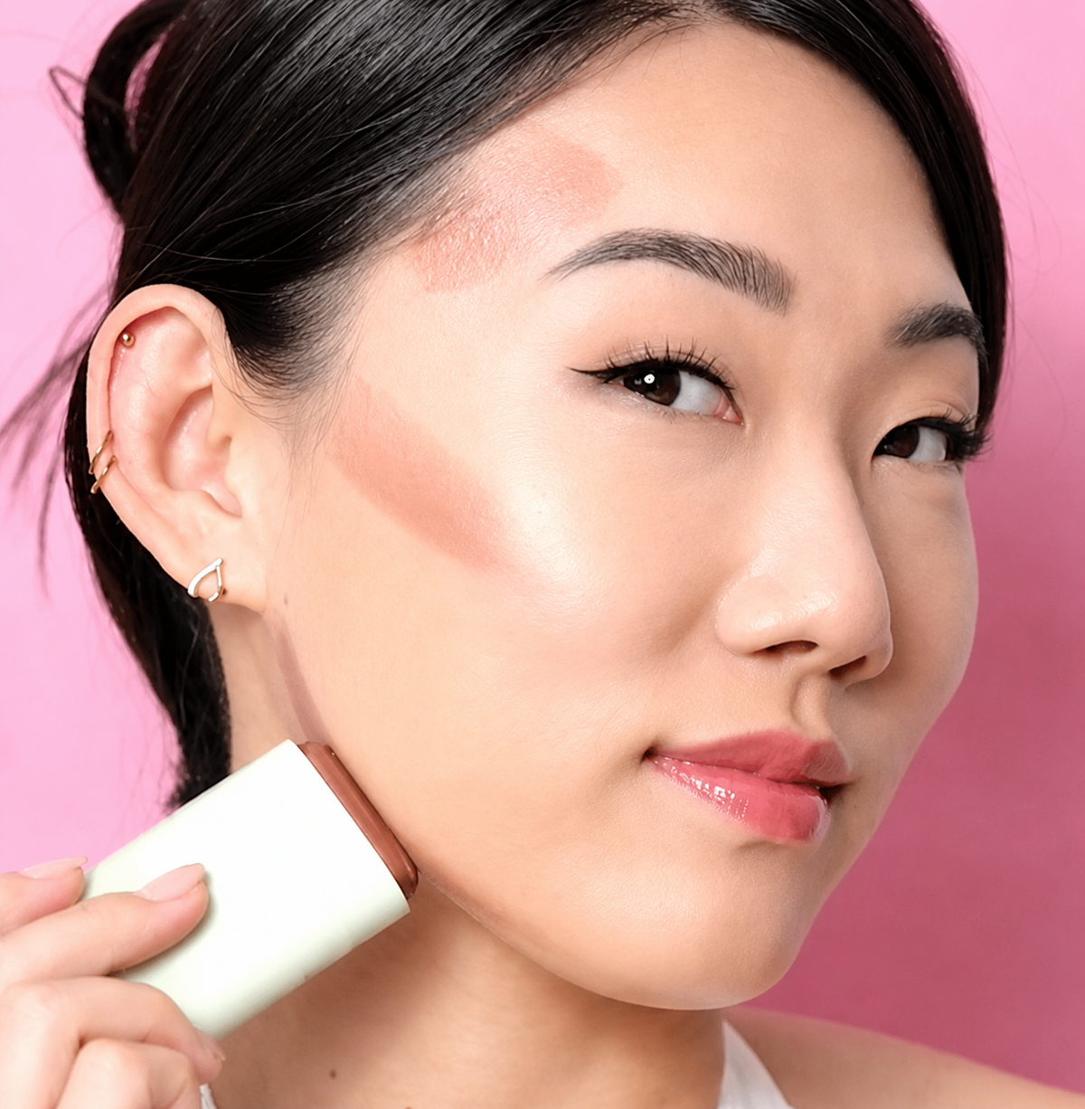 Woman applying On-the-Glow Bronze to her face with a pink background