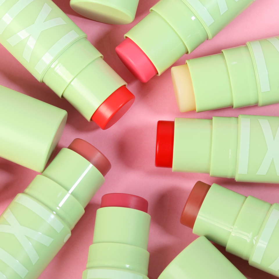 Green and red cosmetic sticks scattered on a pink background view 2
