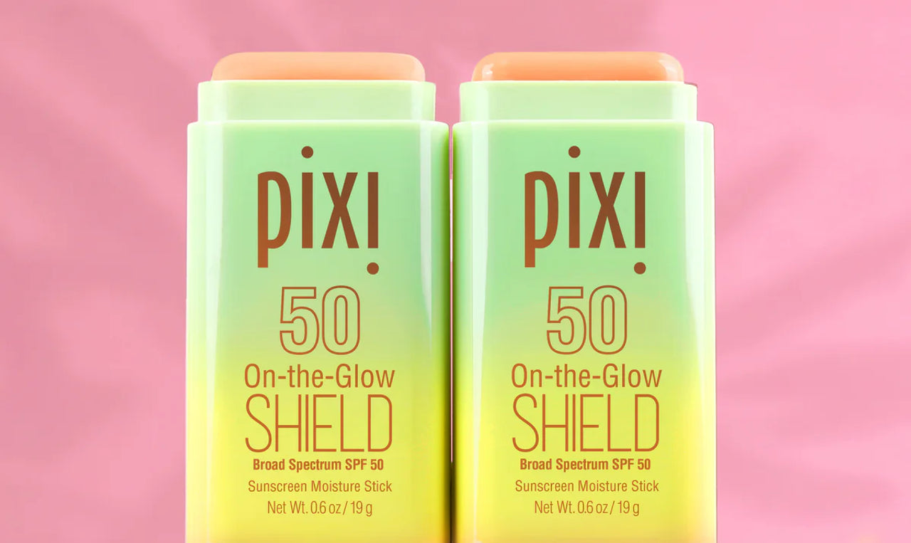Two Pixi On-the-Glow Shield sunscreen sticks on a pink background